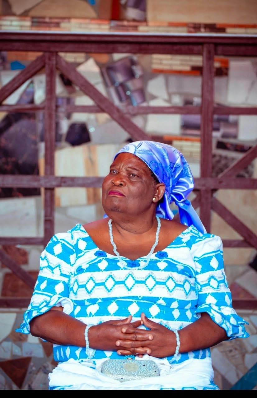 Seated portrait of Esi Nyatepe in a blue and white dress and blue headscarf, hands folded in her lap